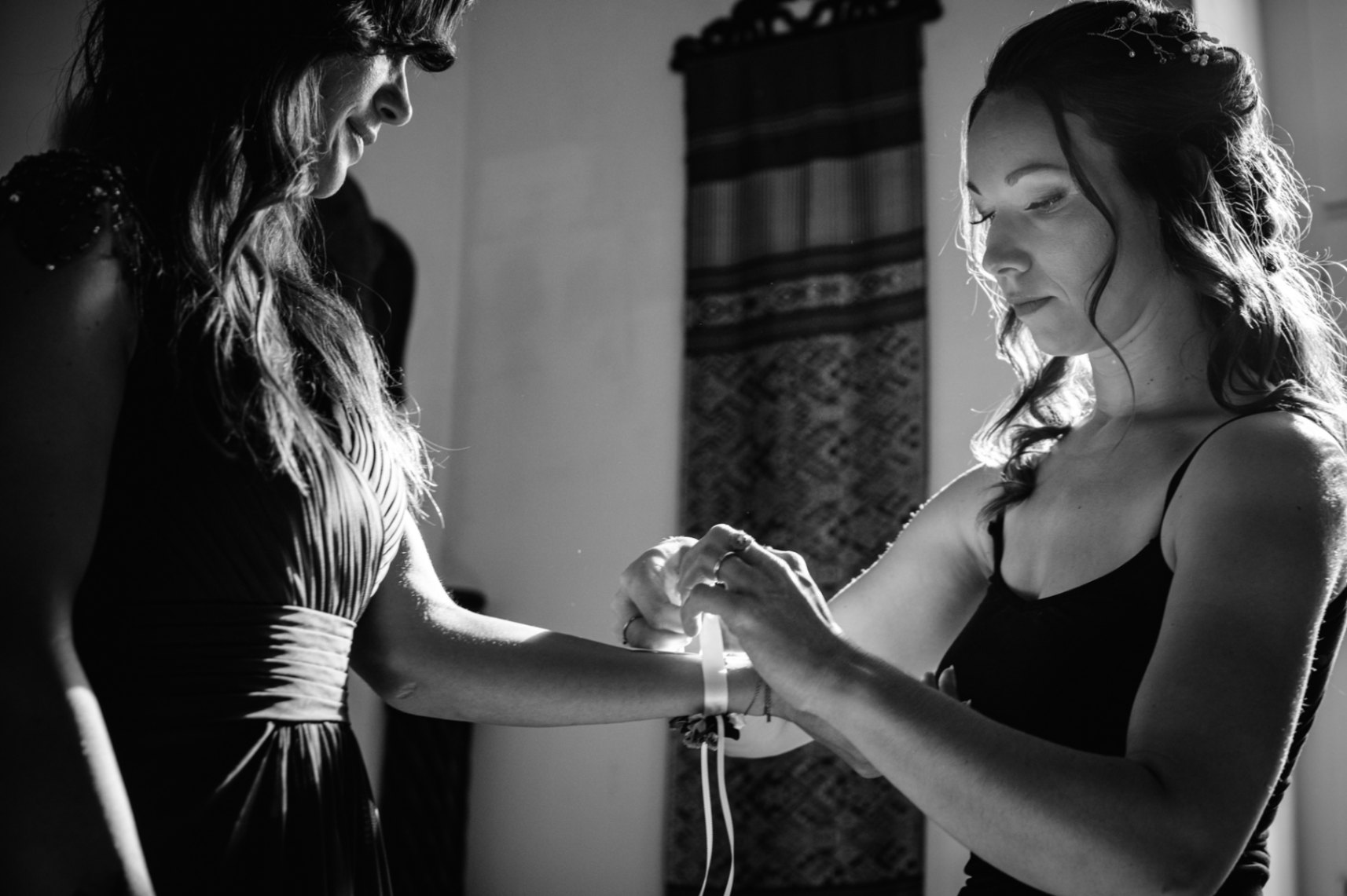 photo de la mariée qui attache une boutonnière au bras de sa témoin